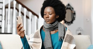 Close up portrait of sick young African American woman sitting at home and talking on video on cellphone. Unwell ill female having video call on smartphone indoors. Disease concept. Healthcare
