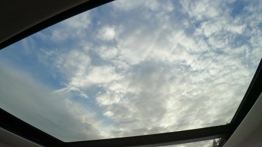 Panoramic glass sun roof in the car. View of the cloudy sky through the open hatch of the car. Royalty-Free Stock Footage #1061473918