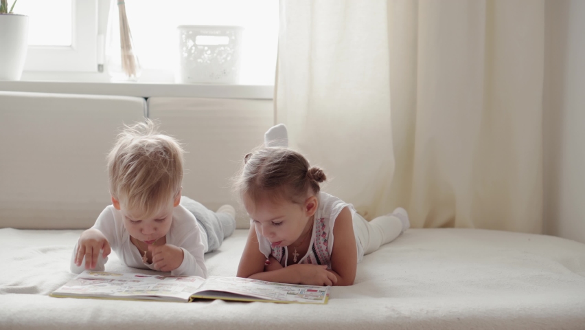 Kiev, Ukraine - 2020.10.15: family concepts - Two smiling children read large interesting book of fairy tales on bed. Siblings little boy and girl brother, sister have fun on quarantine at home | Shutterstock HD Video #1061474662