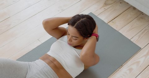 Abdominal muscles training. Top view at focused african american lady doing crunches exercise, lying on floor at home, slow motion
