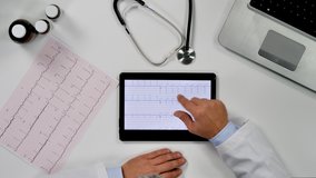 top view of doctor hands examining ecg electrocardiogram at office desk,health care medical,checking exam on digital screen tablet
