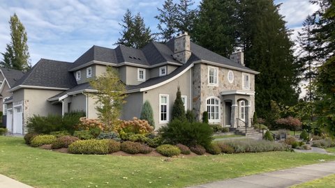 Establishing shot of two story stone and stucco luxury house with garage door, big tree and nice landscape in Vancouver, Canada, North America. Day time on September 2020. Still camera view. H.264.