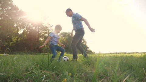 father and son playing football soccer in the park on the grass. happy family dream kid concept. dad and boy play ball outdoor sports in the park healthy. parent lifestyle plays with son into ball