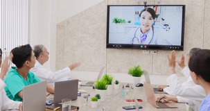 asian young woman doctor chatting to medical team using online video chat on tv screen