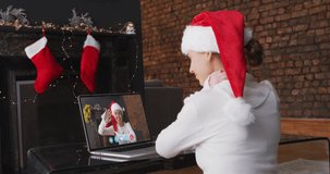 Caucasian woman spending time at home wearing santa hat, sitting by fireplace having video chat with friend on laptop screen, in slow motion. self isolation at christmas time during covid 19 pandemic.