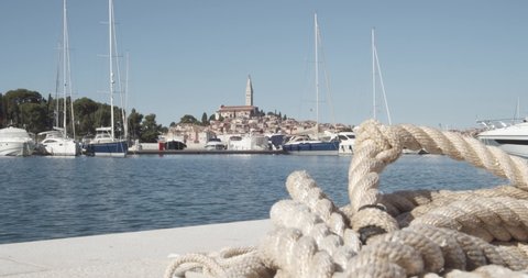 Close up shot of ship rope lying on ground with luxury boats and Rovinj Island in background.Static shot of small croatian city.