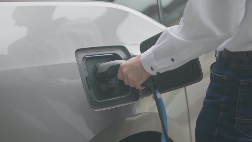 Close up of a modern electric car charger being attached to a silver electric car by a male person wearing a white shirt. Shot in slow motion in 4K. Royalty-Free Stock Footage #1061484922