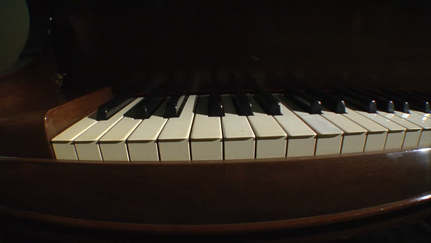 A dim-lit dolly shot of piano keys playing on their own.