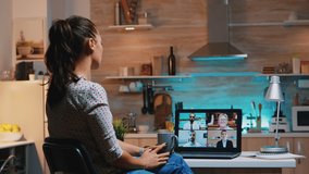 Woman falling asleep during video conference on laptop working from home late at night in the kitchen. Using modern technology network wireless talking on virtual meeting at midnight doing overtime