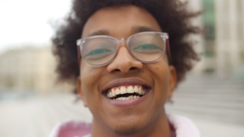 Young handsome african american man wearing casual clothes smiling happy. Close up portrait of cheerful afro teen in glasses looking at camera standing outdoors over blurred background