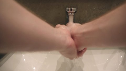 A man washes his hands with soap and water in a public toilet, protecting against myrobes and covid-19 infections. Cleanliness and hygiene, close-up, subjective camera. POV, first poit of view