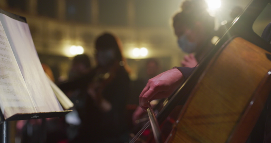 Cinematic Close Up Shot of Symphony Orchestra Cello Player Wearing Medical Protective Mask on Classic Theatre with Curtain Stage during Music Concert. Performers Playing Music for Audience Royalty-Free Stock Footage #1061493634
