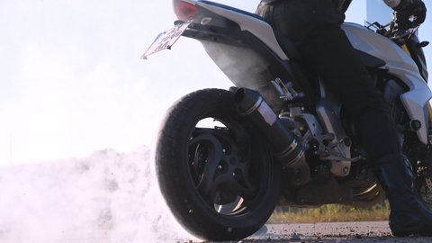Wheel of sport motorbike starting to spin at asphalt and kicking up pebbles and dirt. Biker performing tire burnout with lots of smoke. Motorcycle starts the movement. Slow motion Close up