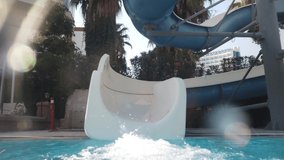 Slow motion video of young girl riding on water slide at aquapark and falling under water in swimming pool