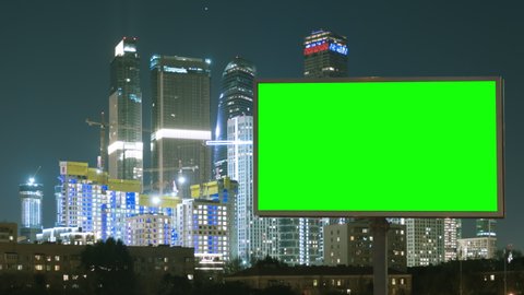 Large billboard with a green screen, a megapolis neon lights with skyscrapers on background, timelapse at night