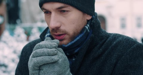 Close up portrait of adult handsome caucasian man in winter clothes standing outside freezing rubbing hands in gray mittens.