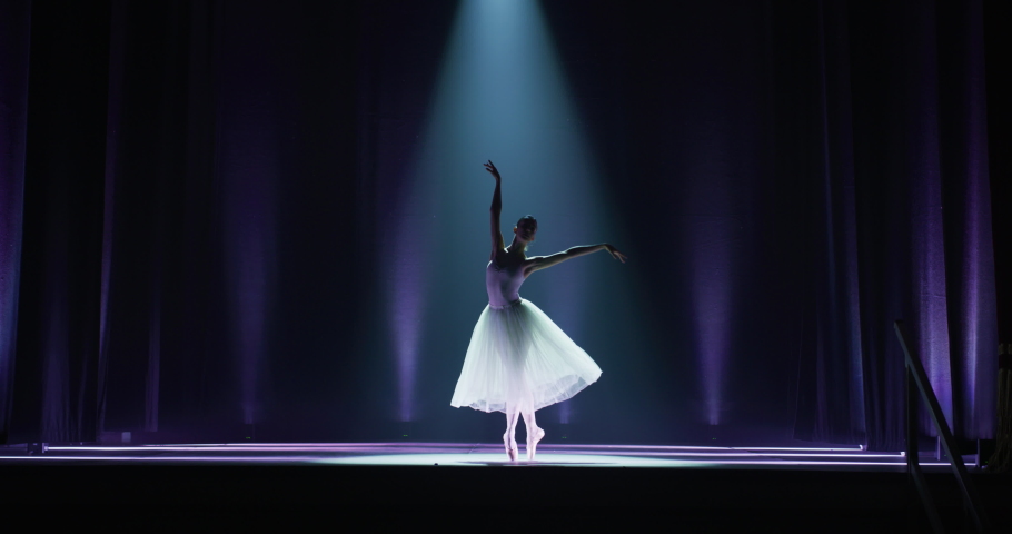 Cinematic shot of an young graceful classical ballet female dancer in white tutu is performing a choreography on classic theatre stage with spotlights before start of a show. Royalty-Free Stock Footage #1061504233