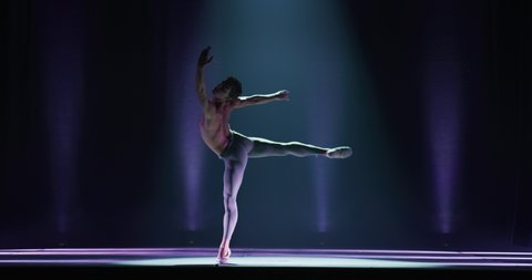 Cinematic shot of an young athletic classical ballet male dancer is performing a choreography on classic theatre stage with spotlights before start of a show.