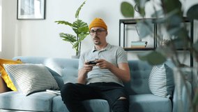 Young man hipster is playing video game holding joystick enjoying hobby indoors at home. Modern devices and entertainment for youth concept.