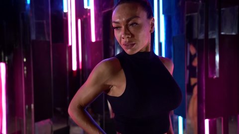 Close-up body of a muscular bodybuilder Dark-haired woman posing and walking in black underwear on a bright neon background in the Studio. The sight of her firm buttocks.