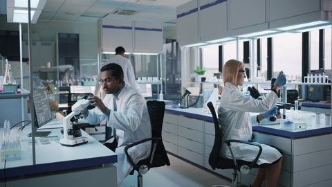 Team of Medical Research Scientists Conduct Experiments with Help of Microscope, Test Tubes, Micropipette and Writing Down Analysis Results on a Computer. Modern Biological Applied Science Laboratory.