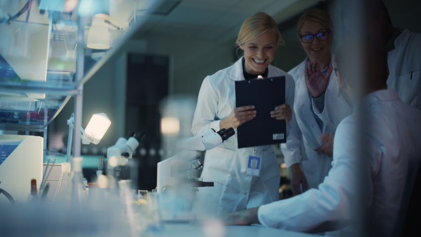 Surprized Male Reseach Scientist Makes an Important Discovery While Researching Samples Under the Microscope. Happy Colleagues Give High Five and Share Success with Fellow Bioengineers. Royalty-Free Stock Footage #1061506336