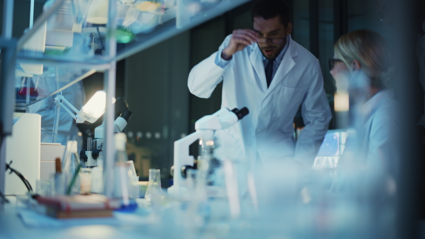 Surprized Female Reseach Scientist Makes an Important Discovery While Researching Samples Under the Microscope. Happy Colleagues Give High Five and Share Success with Fellow Bioengineers. Royalty-Free Stock Footage #1061506339
