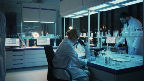 Medical Research Scientist Looks at Biological Samples Under Digital Microscope in Applied Science Laboratory. Beautiful Caucasian Lab Engineer in White Coat Working on Vaccine and Medicine.