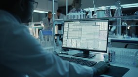 Medical Research Scientist Typing Sophisticated Coding on His Desktop Computer in a Biological Applied Science Research Laboratory. Lab Engineers in White Coats Conduct Experiments in the Background. - Powered by Shutterstock - Get 15% off with code: PIKWIZARD15