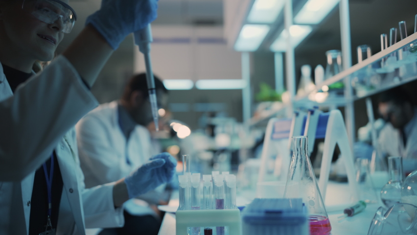 Close Up of a Female Research Scientist Using Micropipette to Mix Liquids in a Test Tube in a Modern Laboratory. Scientists are Conducting Research with the Help of Microscope and Tablet Computer. Royalty-Free Stock Footage #1061506522