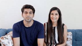 Young boyfriend-girlfriend happily greeting their friends over a group video chat. Point of view shot of an attractive Indian couple in casual wear talking on a video call at home - lifestyle concept