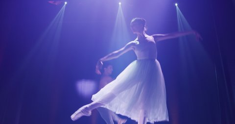 Cinematic shot of young couple of classical ballet dancers is performing a choreography on classic theatre stage with spotlights before start of a show.