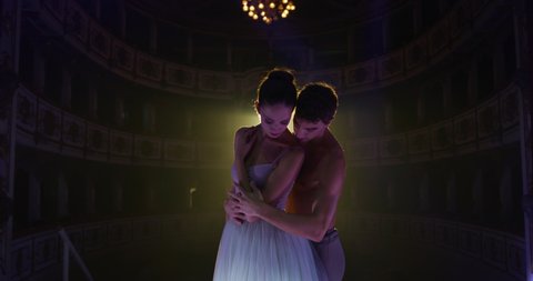 Cinematic shot of young couple of classical ballet dancers is performing a choreography on classic theatre stage with dramatic lighting before start of a show.