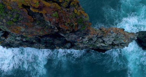 
Aerial vertical view of a separate, steep cliff in the ocean, surrounded by waves. Slow Motion, 4K drone footage. Descent to the top of the cliff. Madeira atlantic coast. Portugal