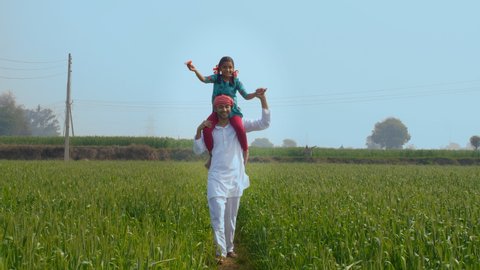 A father-daughter duo enjoying their simple happy life roaming in their farmland. A long shot of a carefree farmer with his little girl on his shoulders - Happy Parenting