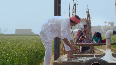 An Indian farmer and his happy village family - Education and Hardwork . A young farmer washing his feet while his wife looking after the studies of their little girl sitting near a field