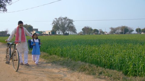 A young village farmer taking his girl child to school. Beti bachao beti padhao. An Indian father and his school-age daughter in uniform - walking on a mud road. Girl child education
