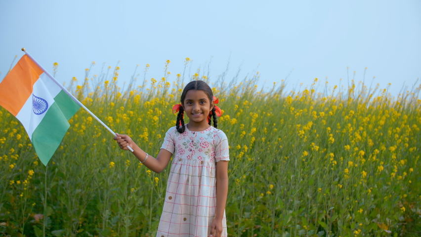 Young village girl proudly swinging the Indian flag while standing in a mustard farm. Medium shot - Indian kid waving the national flag of India on the occasion of Independence Day or Republic Day | Shutterstock HD Video #1061511013