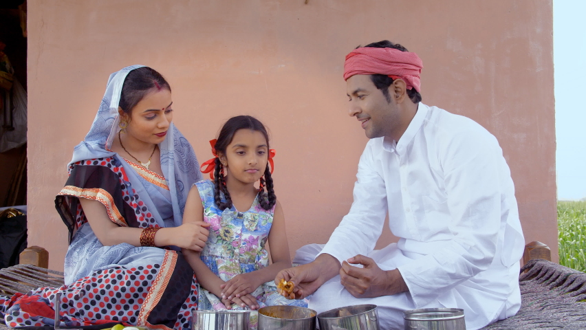 Loving and caring village parents feeding their daughter while sitting on a charpai. Medium shot of an Indian farmer having delicious food with his wife and daughter - village family lifestyle Royalty-Free Stock Footage #1061511052