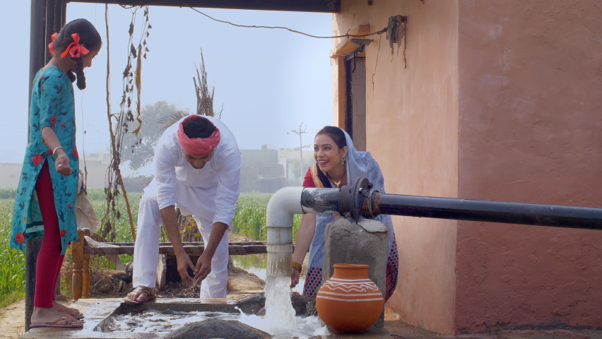 Village couple and their daughter enjoying together on a beautiful summer day. Happy Indian farmer and his small family playing with freshwater near a tubewell - village lifestyle concept Royalty-Free Stock Footage #1061511082