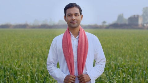 Young attractive farmer happily standing in his field while folding his hands. Medium shot of an Indian boy wearing kurta pajama and safa standing in his village farm