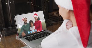 Caucasian woman spending time at home wearing santa hat, sitting by fireplace having video chat with friends on laptop screen, in slow motion.self isolation at christmas time during covid 19 pandemic