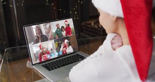 Caucasian woman spending time at home wearing santa hat, sitting by fireplace having video chat with friends on laptop screen, in slow motion.self isolation at christmas time during covid 19 pandemic
