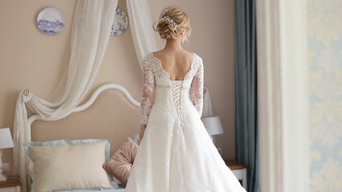 close - up portrait of the bride, rear view. Bride in a chic wedding dress in a home interior. The bride is standing by the big bed with her back to the camera. Wedding concept