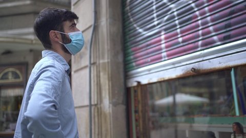 Young business man with mask closing a small local store door during the coronavirus crisis
