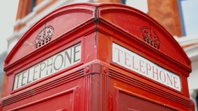 Smooth backward 4k shot of the Top of a London telephone booth with a blurry brick building as background.