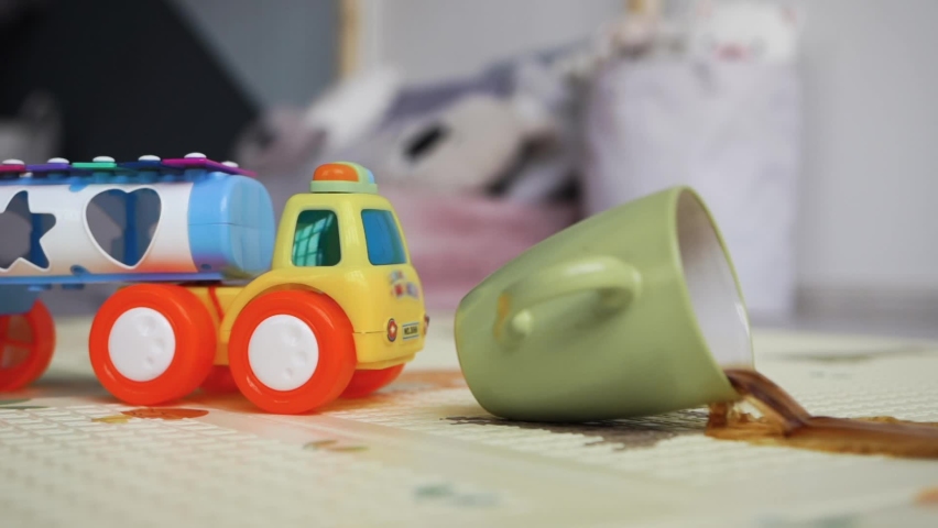 Apartment children room child plays bright toy car crashes drops pours glass coffee tea carpet. Sloppy handling child leprosy. Dirty floor carpet apartment. Kid fidgety. Splashes different directions. | Shutterstock HD Video #1061518609