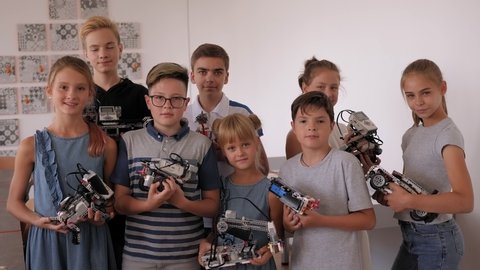 A group of students holds many different robots assembled from plastic parts programmed on a computer in a robotics lesson at school.