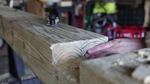 An individual uses a block plane on a woodworking project. Shot from the perspective of his hands.