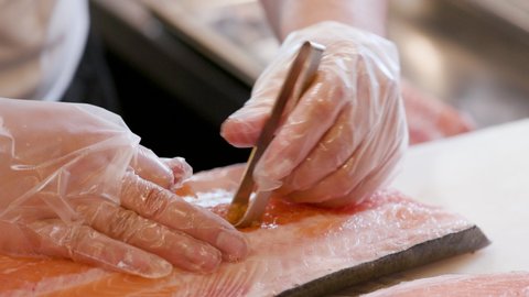 Close up of a chef's hand deboning fresh salmon for a delicious Sushi. Preparing Asian Japanese food in a restaurant kitchen.